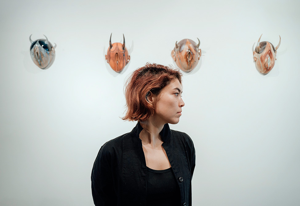 A person's face in profile in front of four masks mounted on a wall