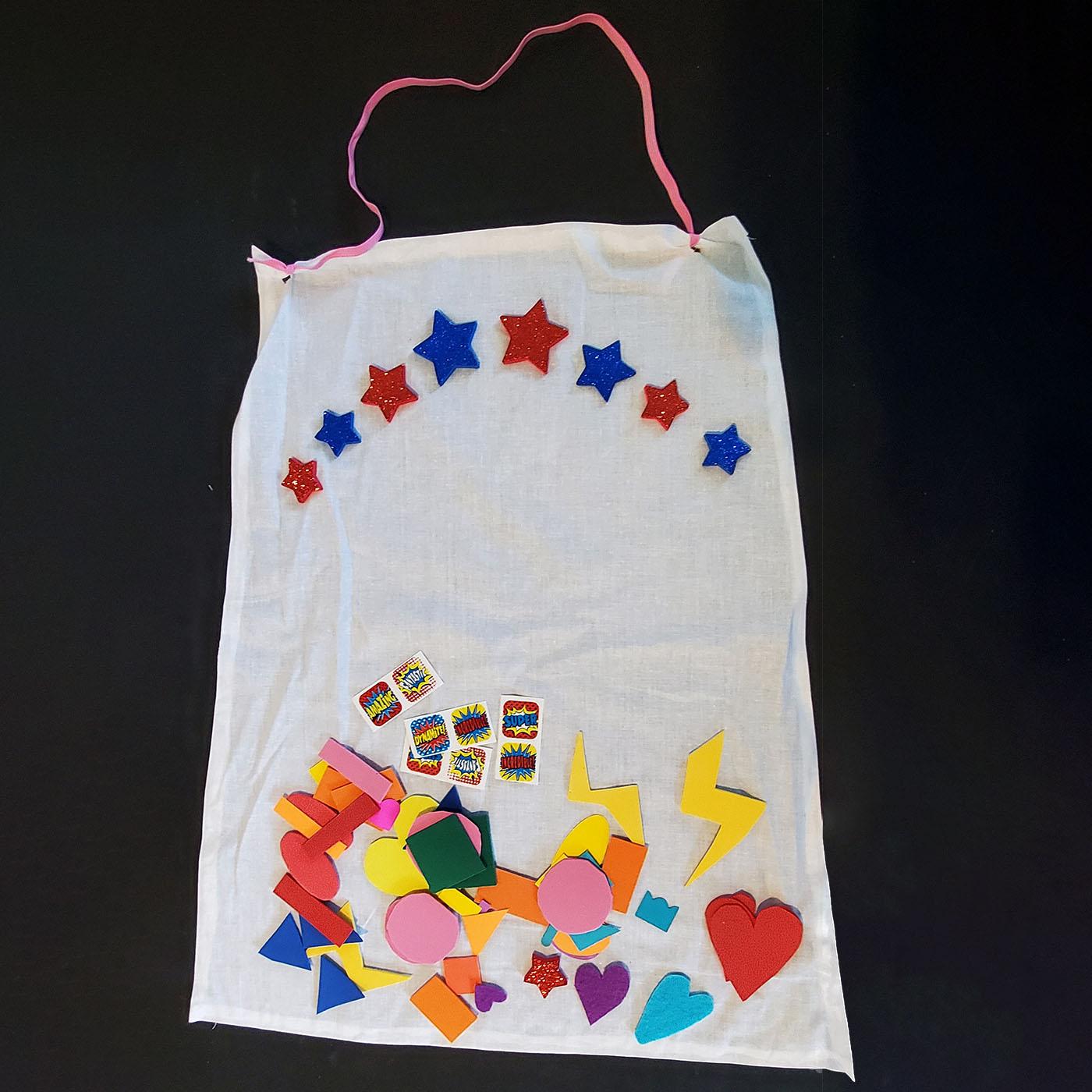 A piece of muslin fabric in the form of a cape with shapes and stickers on top