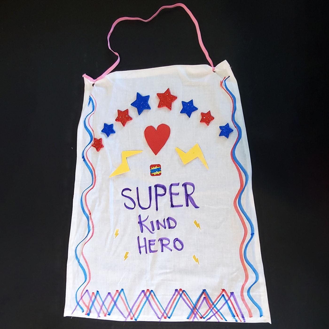 A cape made out of fabric with star decorations and text reading 'Super Kind Hero'