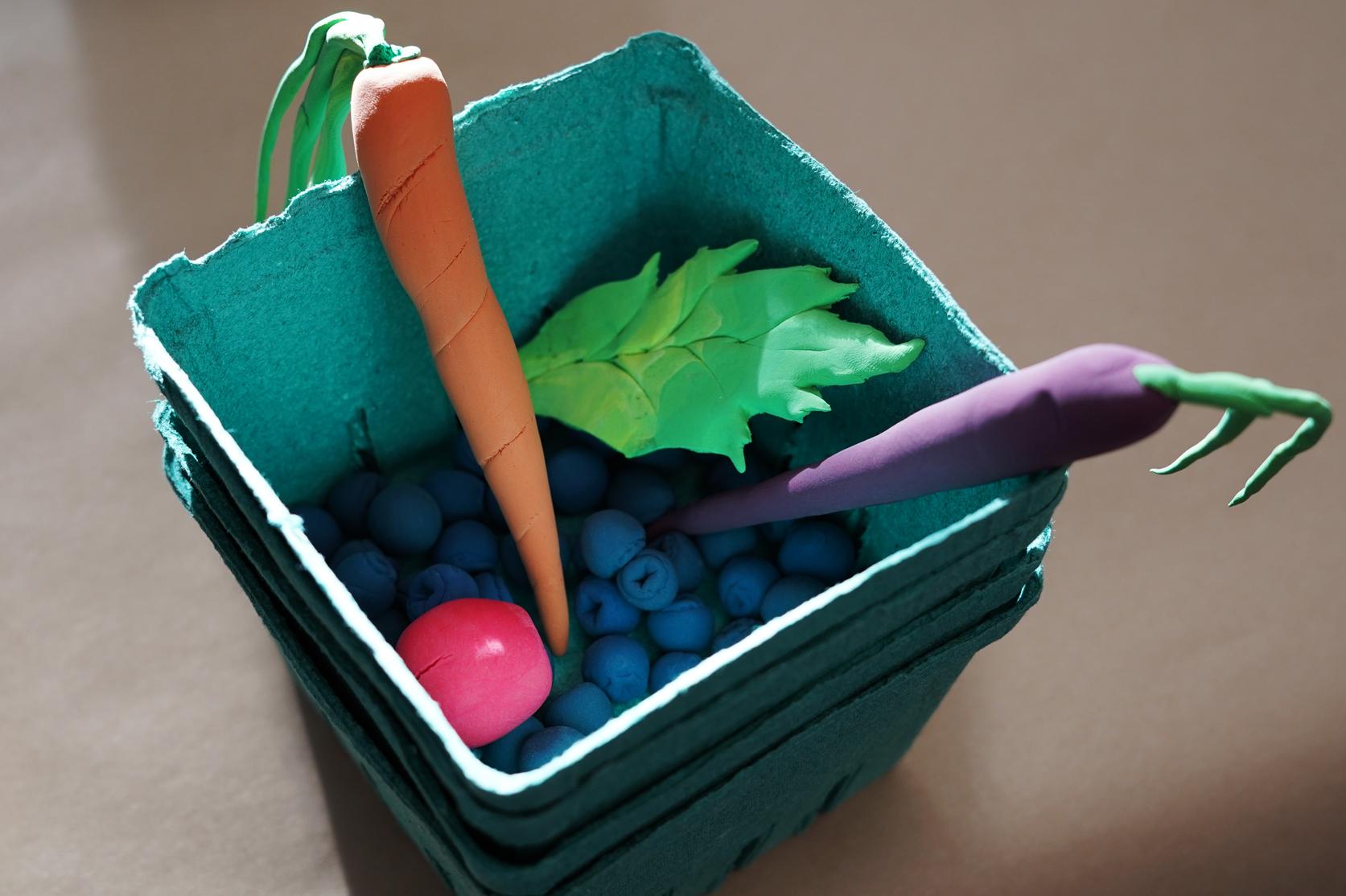 Photo of fruits and vegetables made of modeling clay in a green molded pulp berry basket