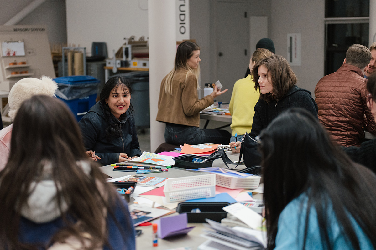 People sitting around a large table covered in art supplies and chatting