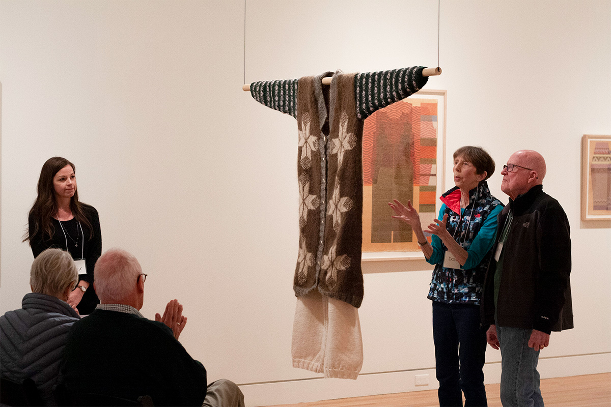 People standing around and talking about a suspended textile artwork