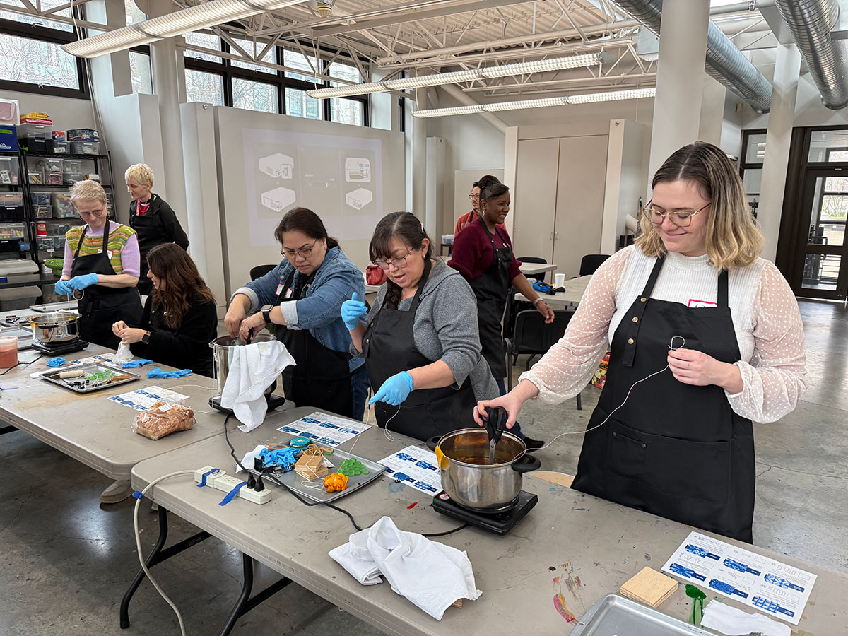 People working on an art project along a long table in a well-lit studio space