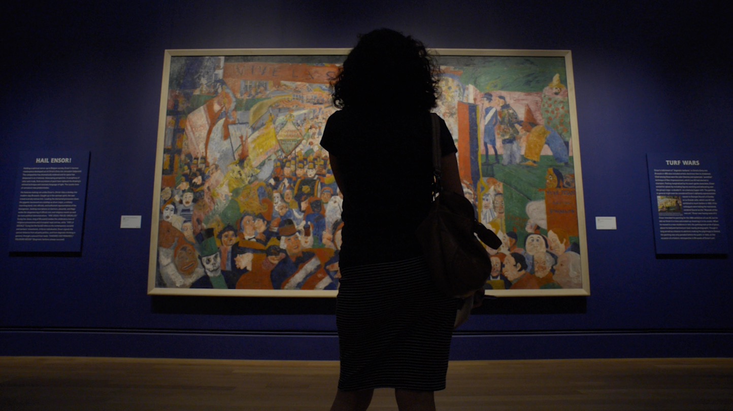 A silhouette of a woman looking at a large artwork hung on a blue wall 