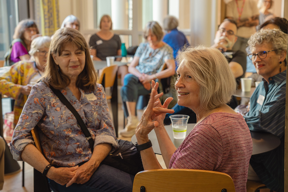 A large group of older adults sitting at tables in a café space and looking at an unseen speaker