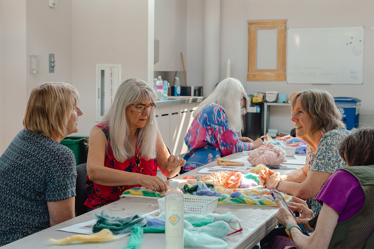 A group of older people at a long table working on an art project with colorful fabric
