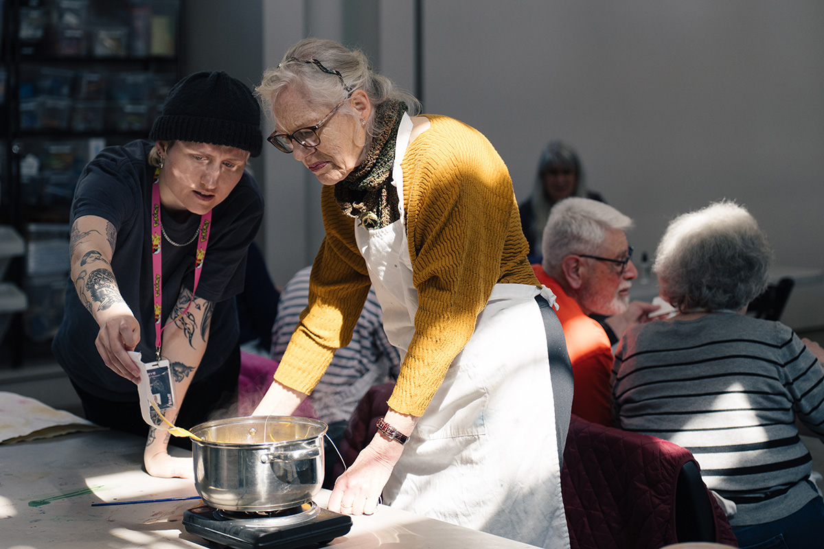 An older and younger person lean over a pot heating liquid for an art dyeing project