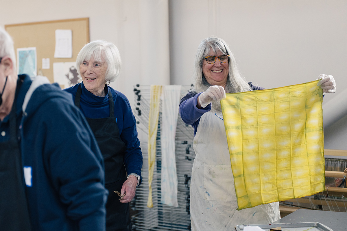 People smiling and looking at a freshly dyed yellow handkerchief