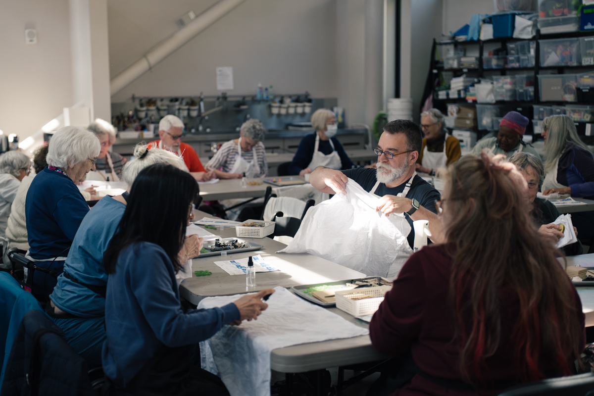 Older adults sitting at long tables with art and craft supplies