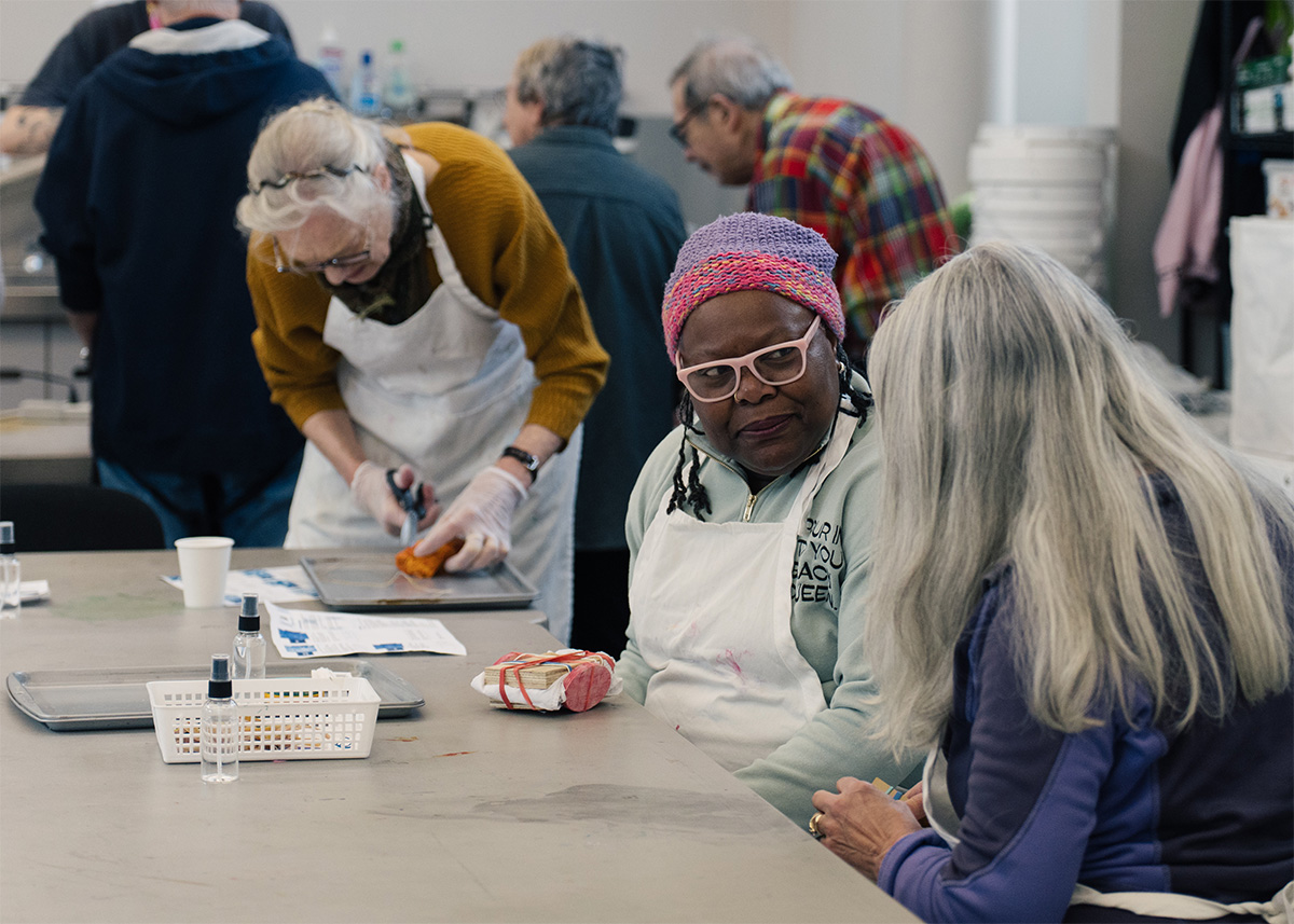 People chatting at a table while other people behind them work on art projects
