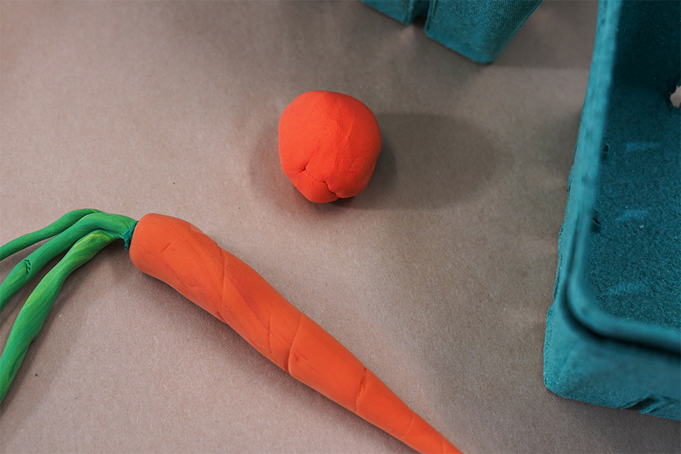 A carrot made of clay next to a ball of clay ready to be shaped into another vegetable