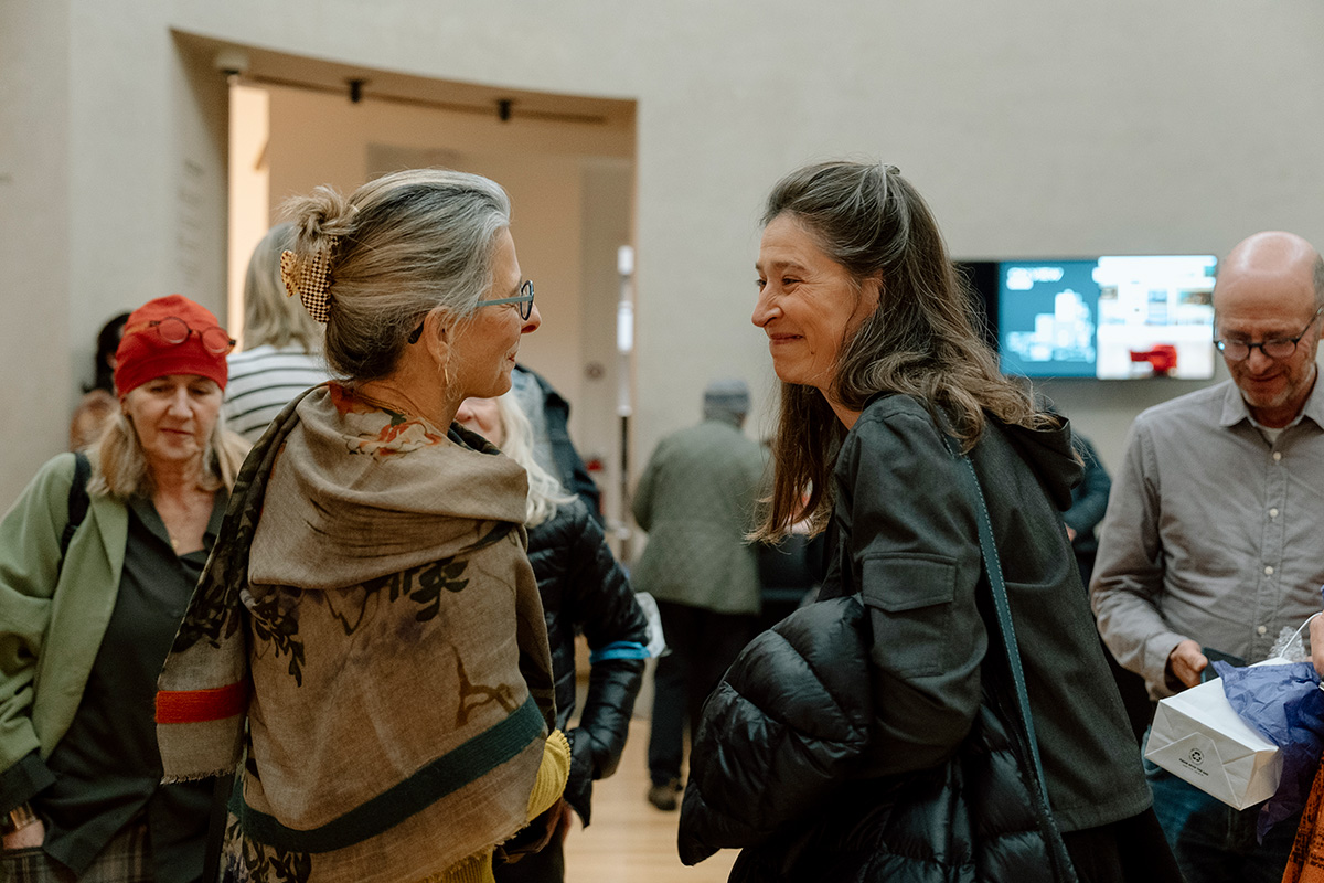 People in jackets smiling and greeting each other in a large rotunda space. There are more people in the background entering.