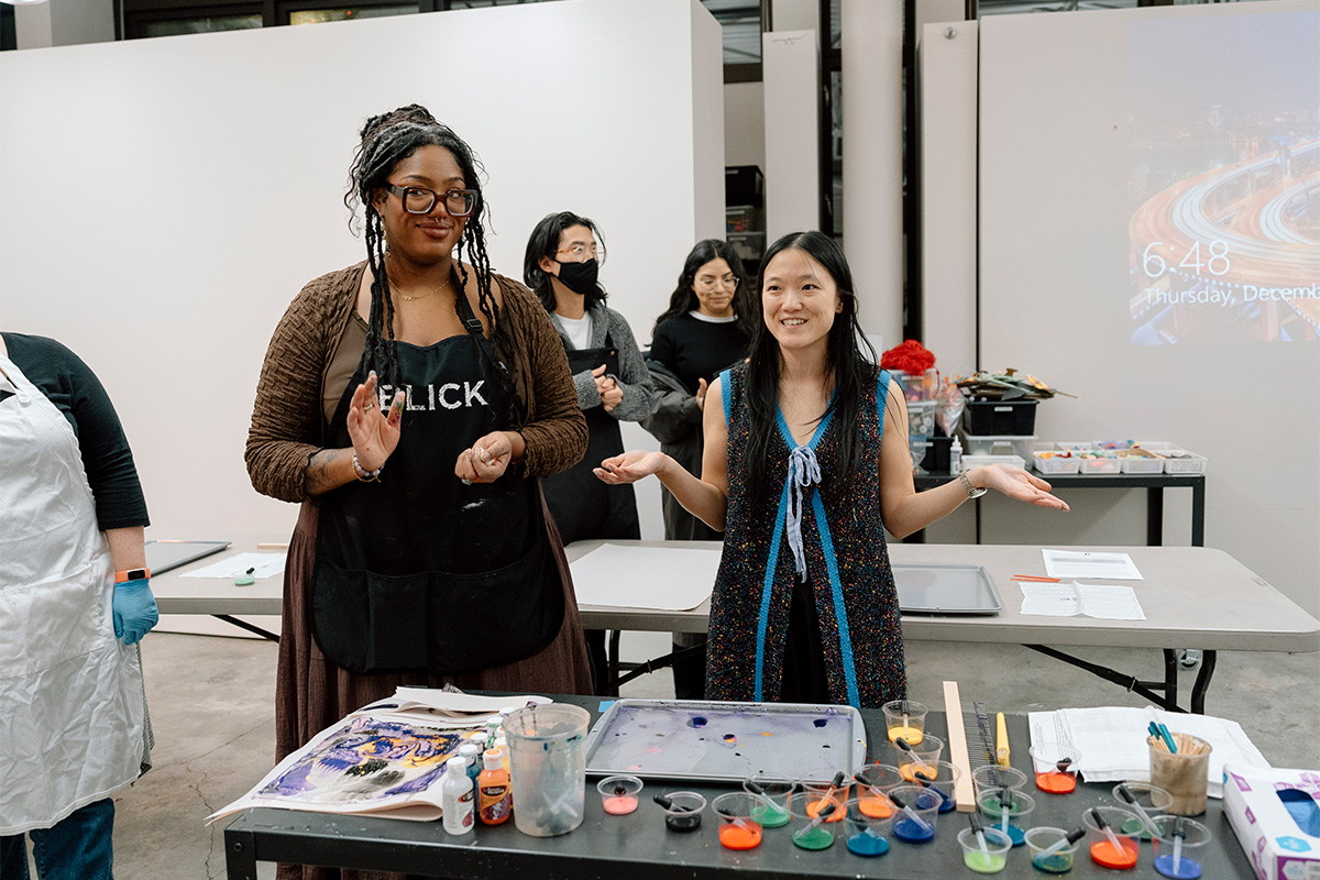 People standing behind a table covered in art supplies in a studio space