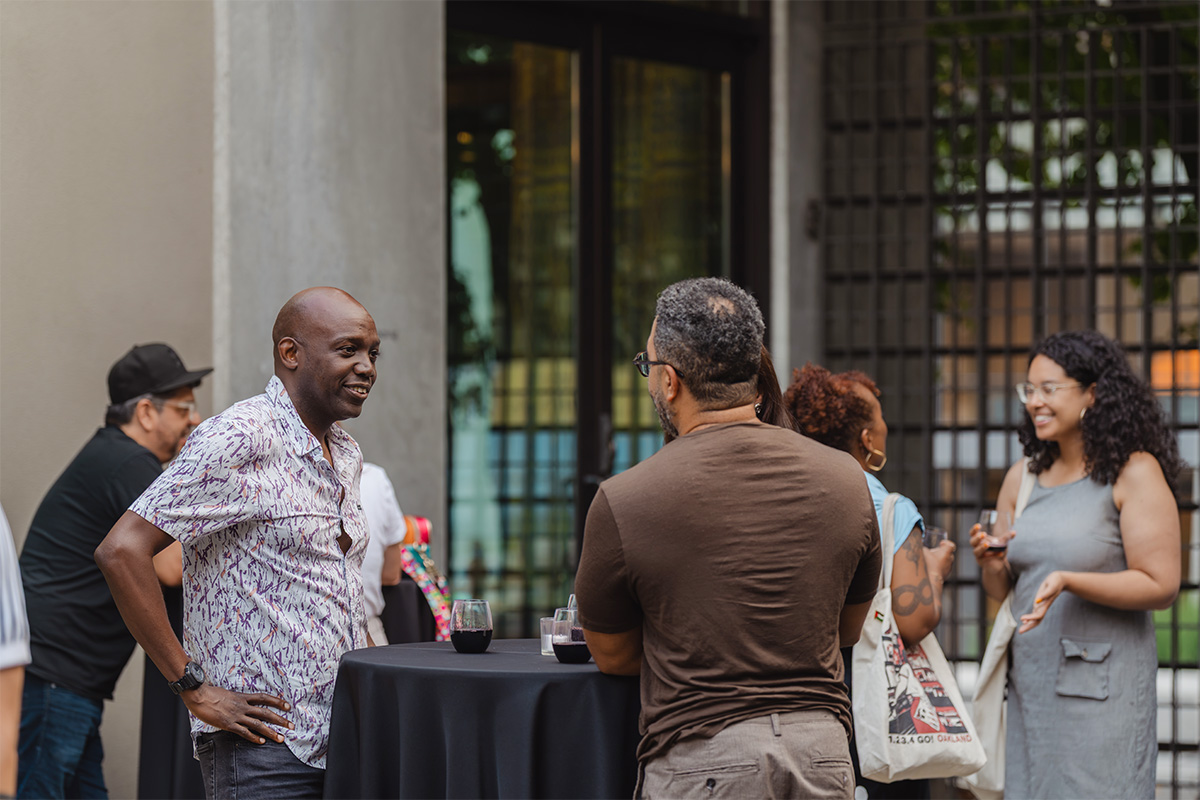 People in an outdoor courtyard in the evening standing at tall tables with drinks and chatting