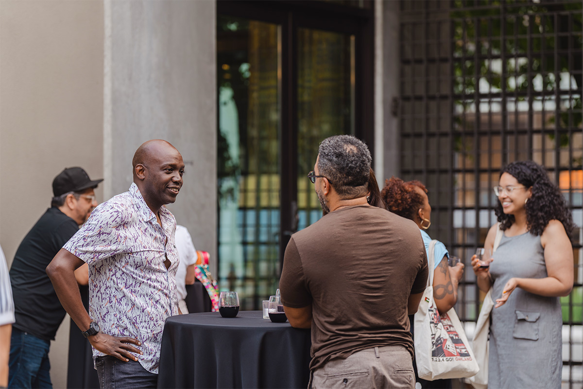 People in an outdoor courtyard in the evening standing at tall tables with drinks and chatting