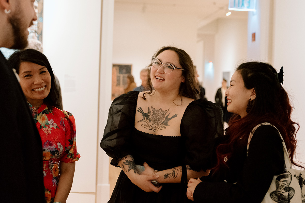 A small group of people in dresses and nice clothing smiling and chatting in a museum gallery space