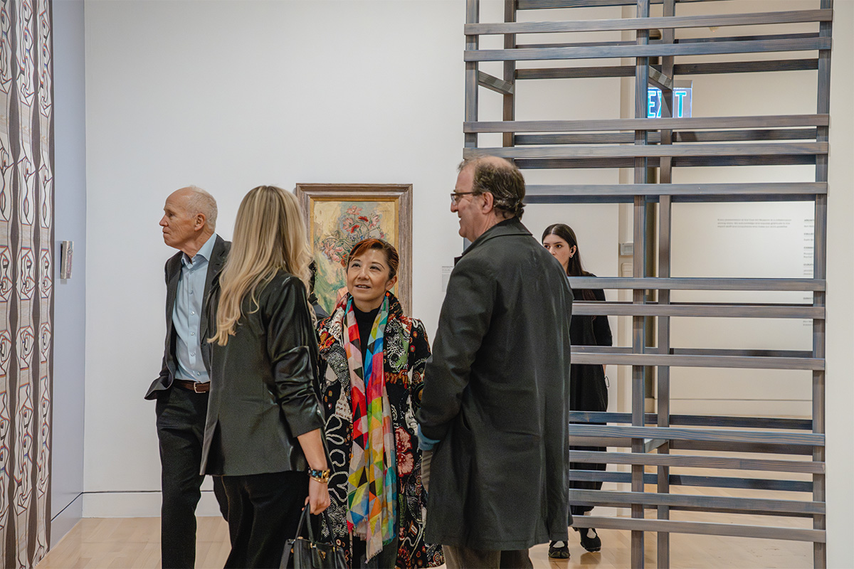 A group of three people chatting in a gallery space. There are others moving through the gallery behind them.