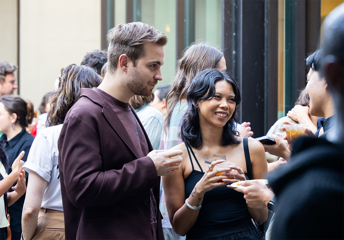 People standing, smiling, and chatting in a sunny courtyard while holding drinks