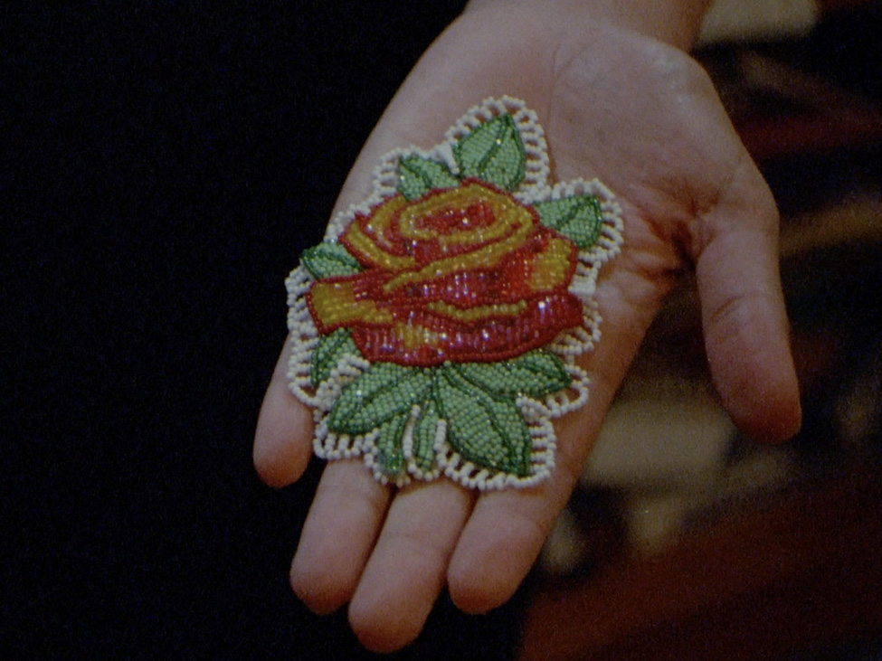 A still from a video of a person's palm holding a beadwork flower