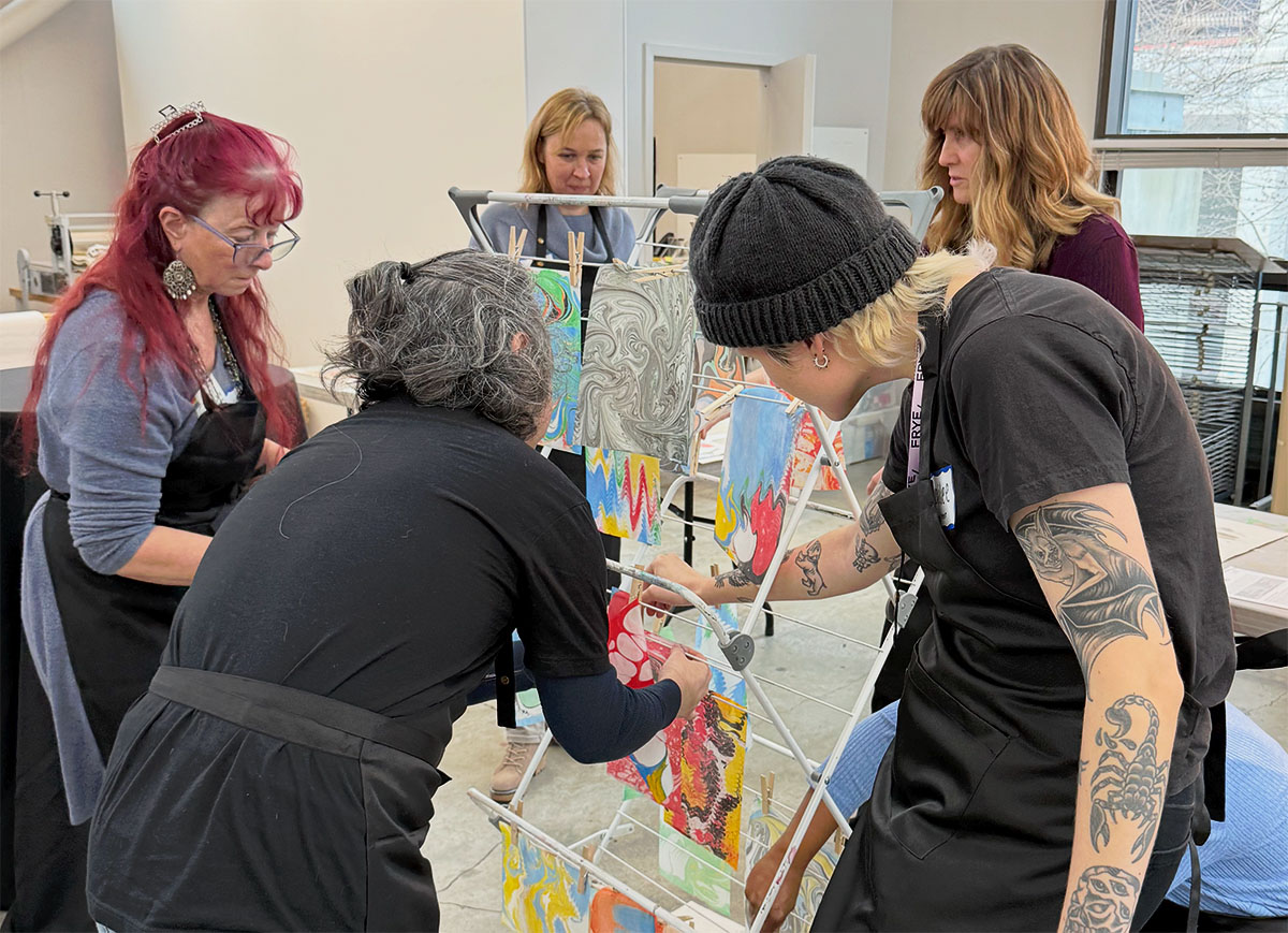 People hanging artworks with wet mediums on a drying rack