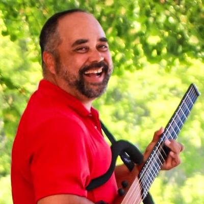 A smiling man in a red shirt holding a guitar