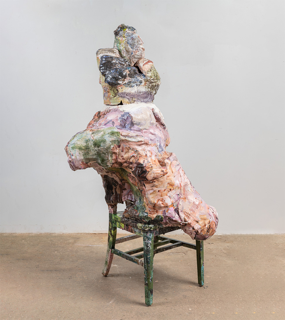 A ceramic and papier-mâché sculpture of a figure sitting on a chair