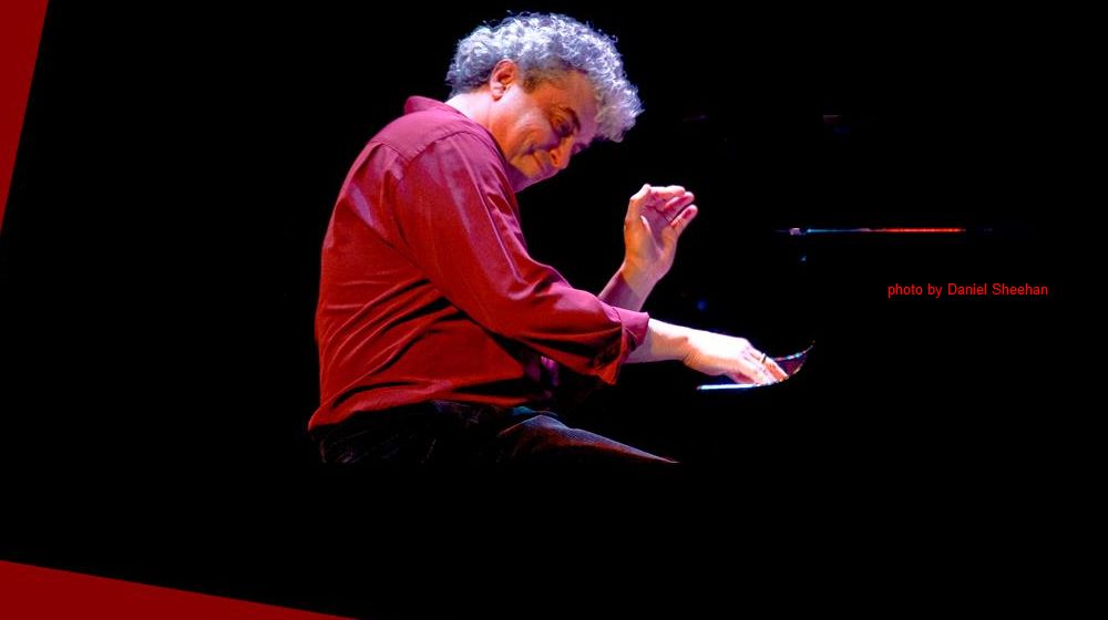 Photograph of Jovino Santos Neto playing a piano with a spotlight on him