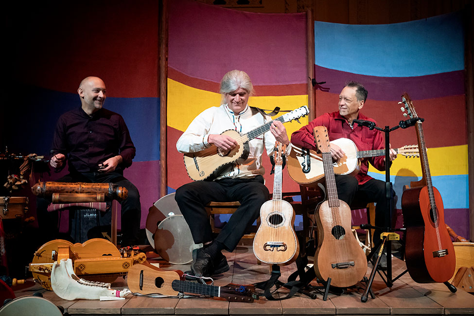 Three musicians on a stage surrounded by instruments