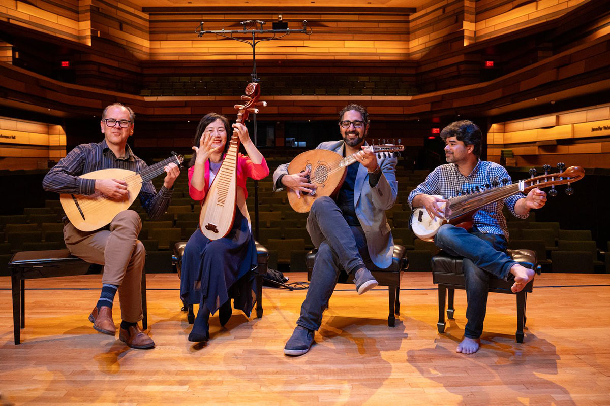 Four people sitting on a stage holding string instruments