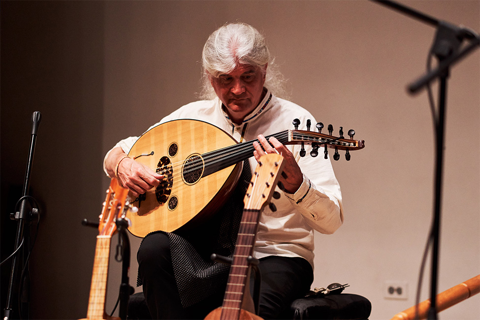 A person playing a lute on stage surrounded by other instruments and music equipment