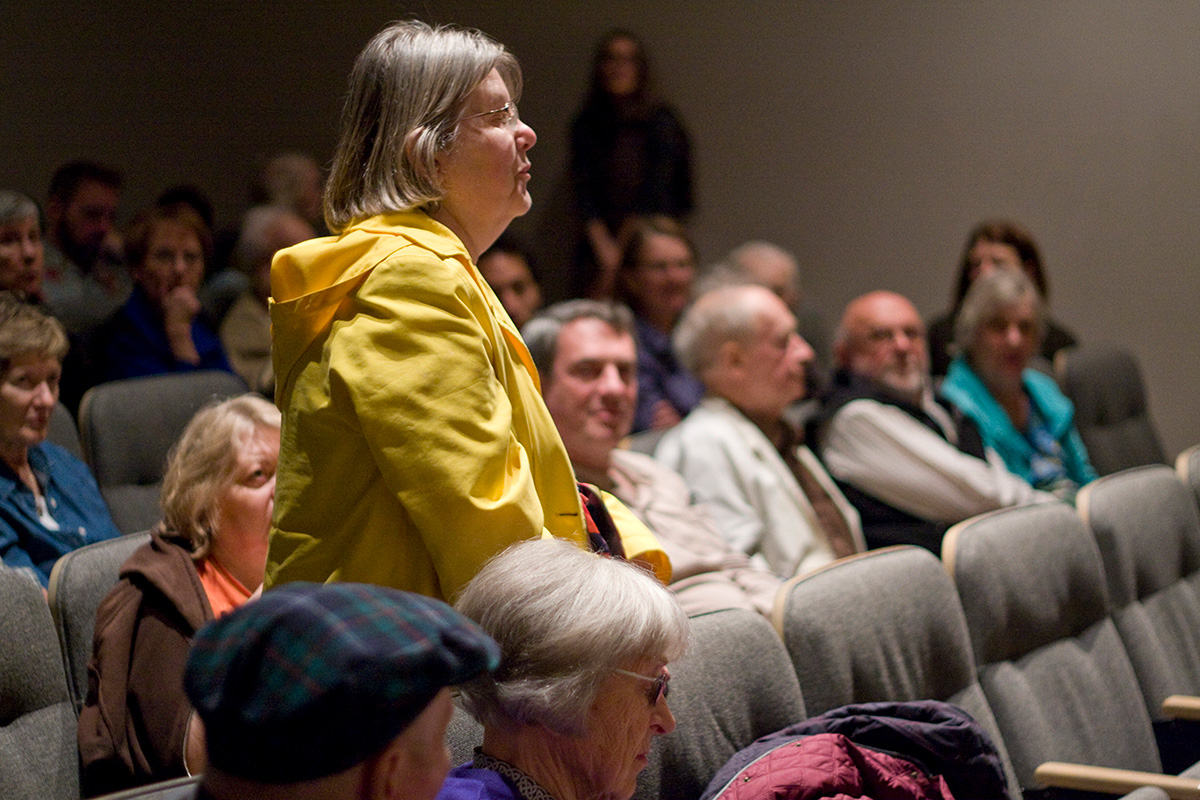 A woman standing to speak in mostly full auditorium seating