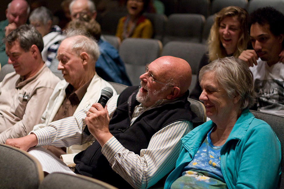 A member of the audience in a theater holds a microphone while sharing a story