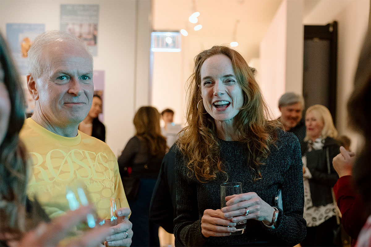 A couple smiling and holding drinks in a moderately crowded room