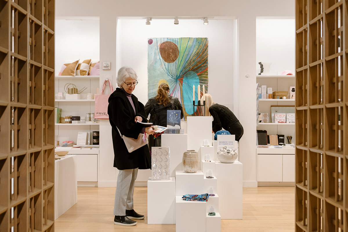 Three people standing and browsing goods in a well-lit museum shop