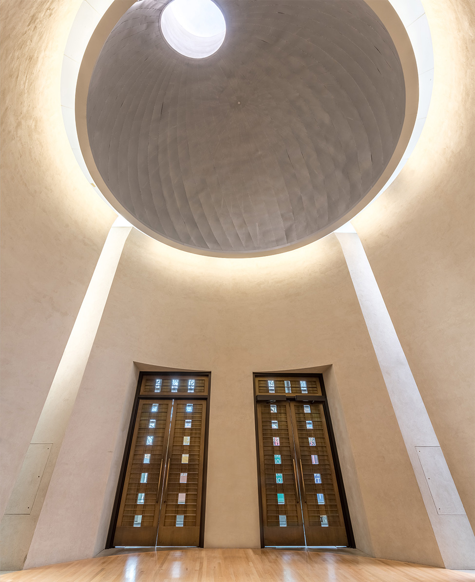 A vertical, wide-angle image of two doors underneath a large, circular rotunda ceiling with an offset skylight