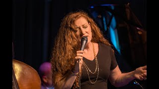 A woman with curly hair and a black top signing into a microphone on stage