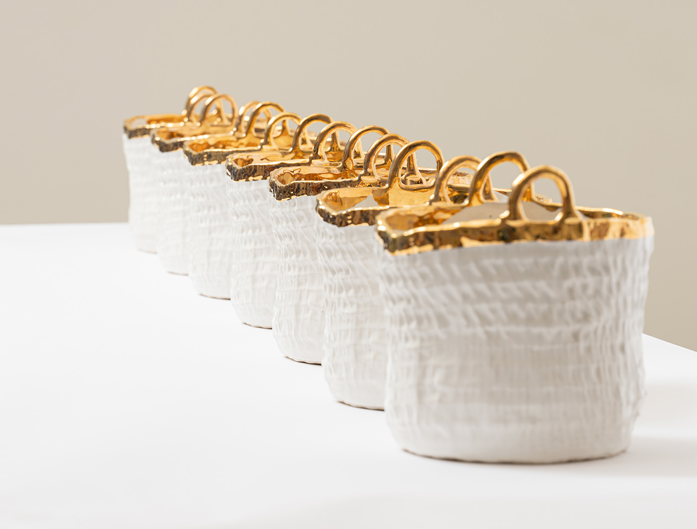 A row of white ceramic baskets with gold accents on the rims and gold handles