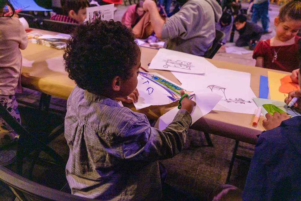 A child cutting a piece of paper while making an artwork at a long table