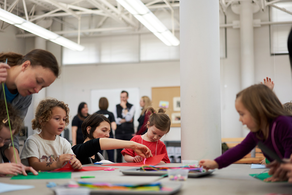 Children and adults engaged in an art activity at a long table