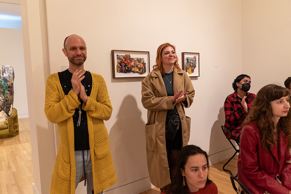 People standing and clapping in front of a wall with small artworks