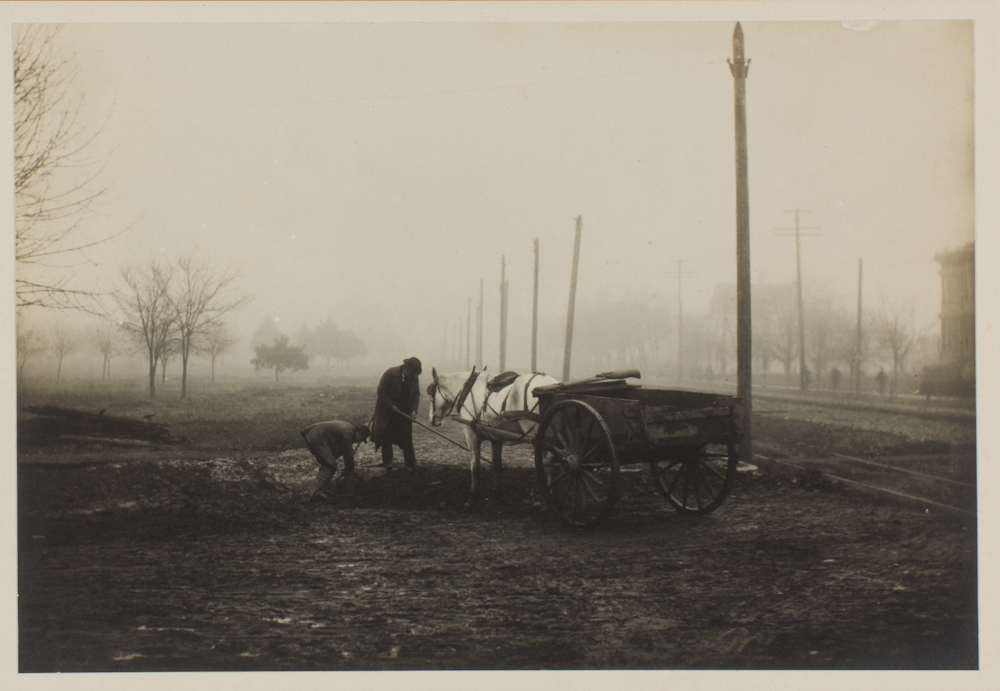 A sepia-toned photograph of two people with a horse pulling a small, open carriage