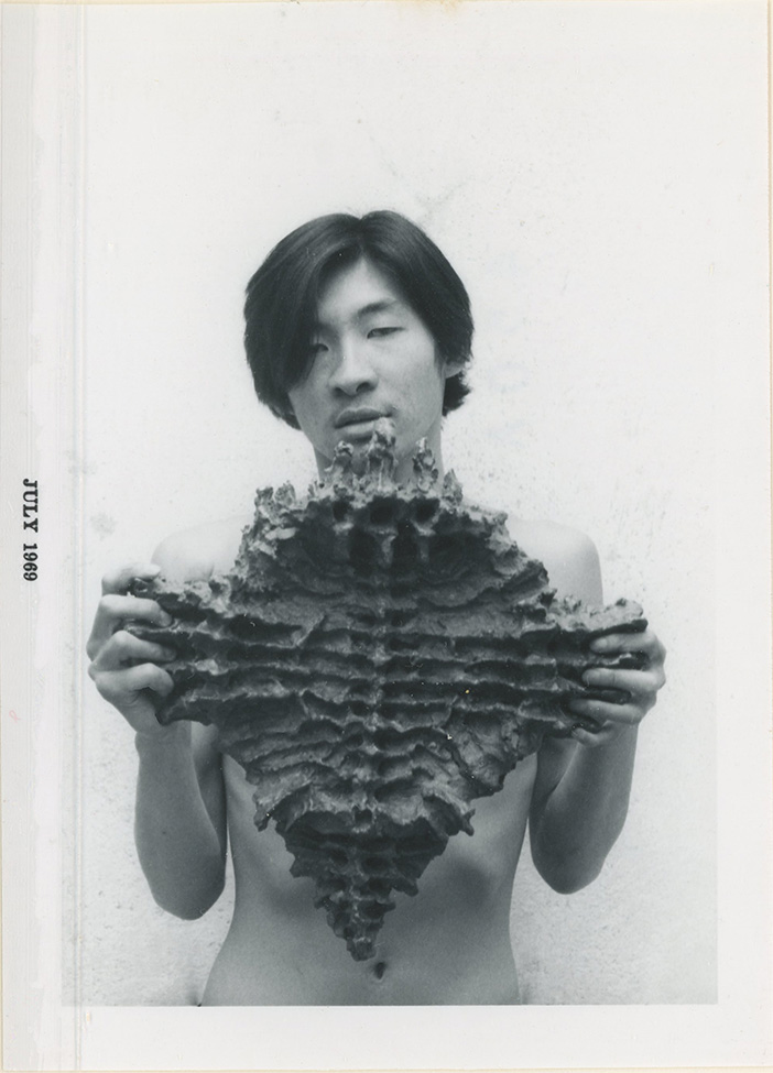 A photograph of a young, shirtless Asian man holding a sculpture