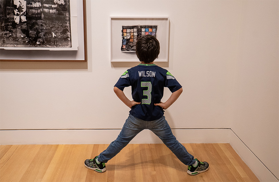 A child standing in front of and looking closely at an artwork on the wall