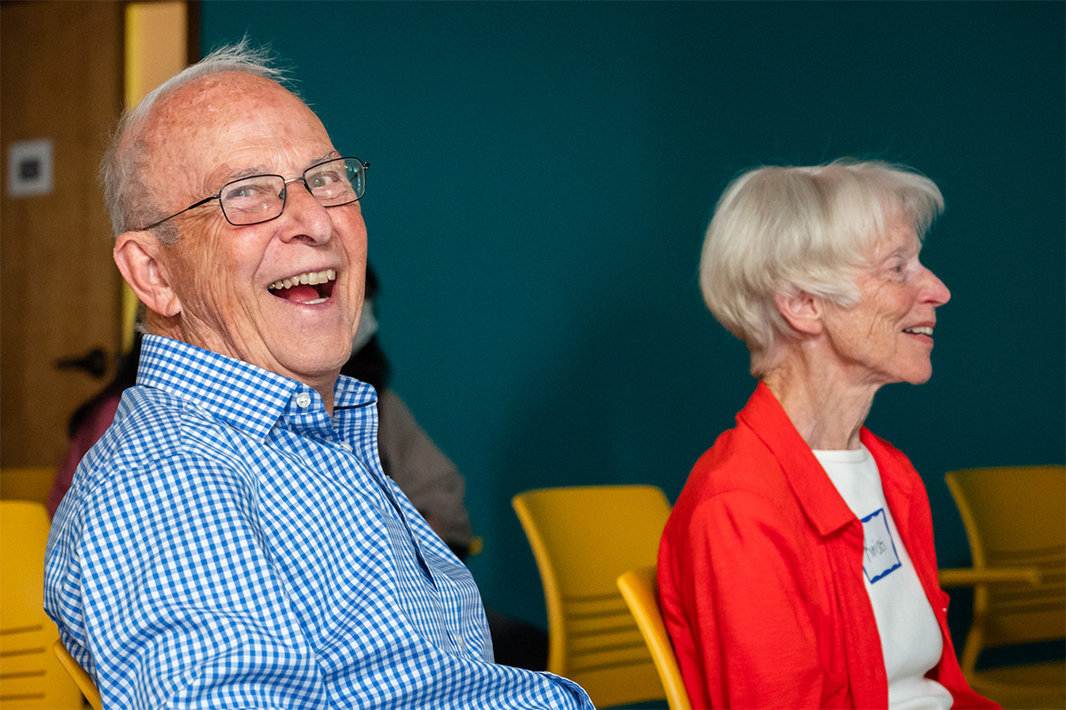 Two seated older people, one is smiling at the camera