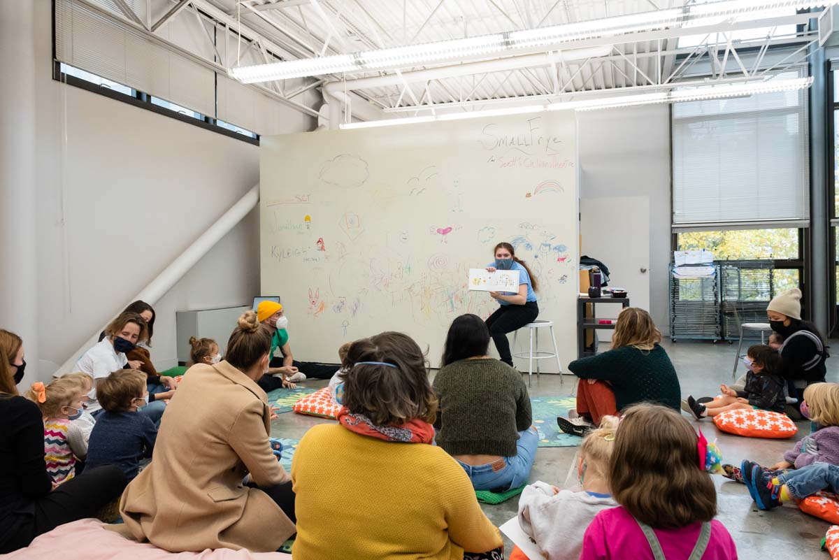 A group of children sitting in the Art Studio listening to an adult reading a book