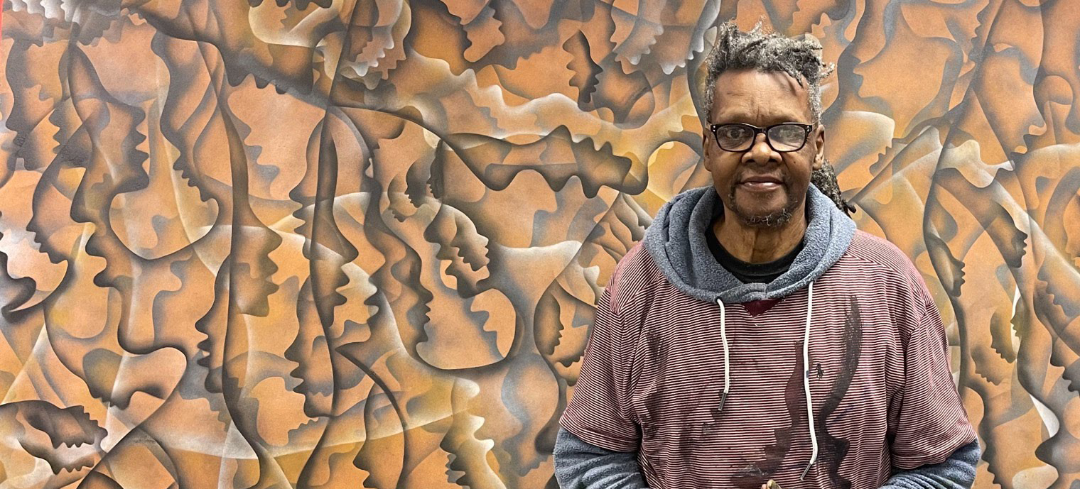 An older black man standing in front of a large, abstract artwork