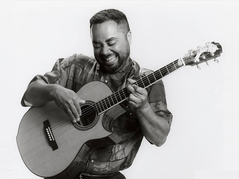 A black and white photo of a man smiling and playing a guitar