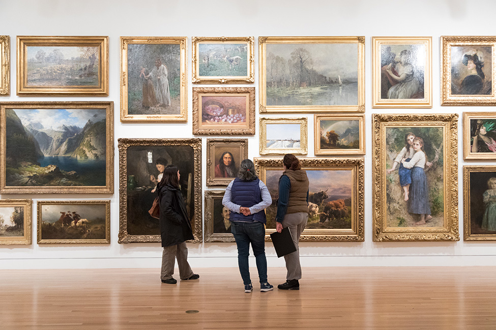 People standing in front of paintings hung salon style at the Frye Art Museum