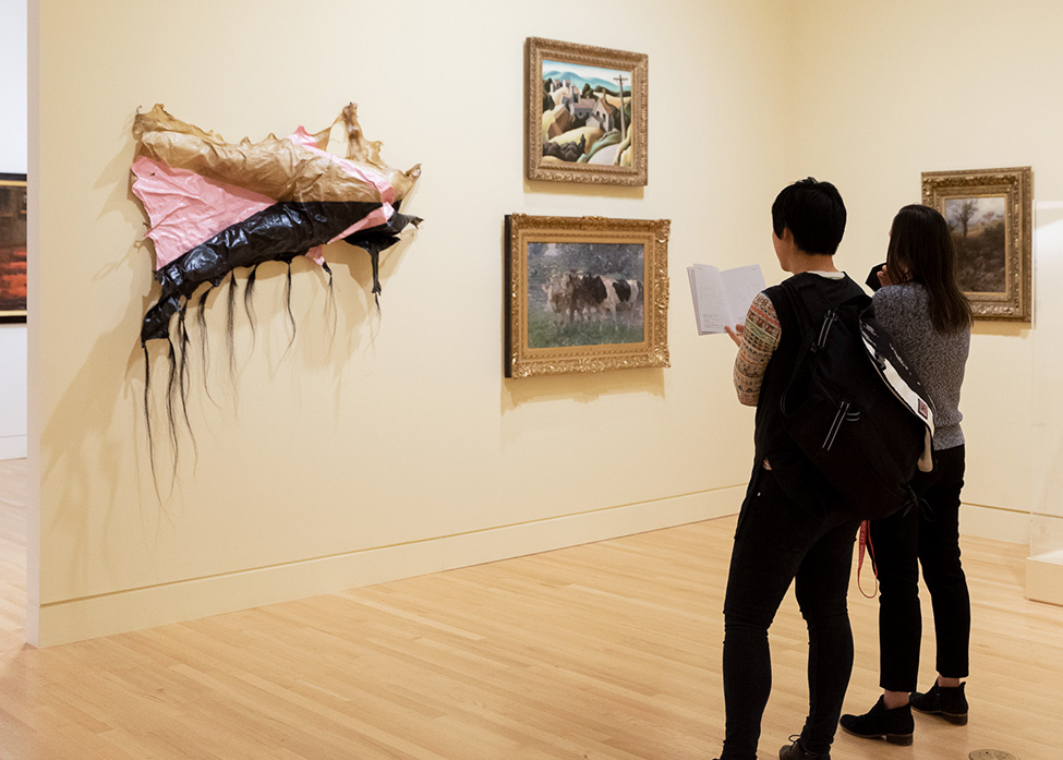 A person reading from a book next to another person standing in the Frye Art Museum galleries