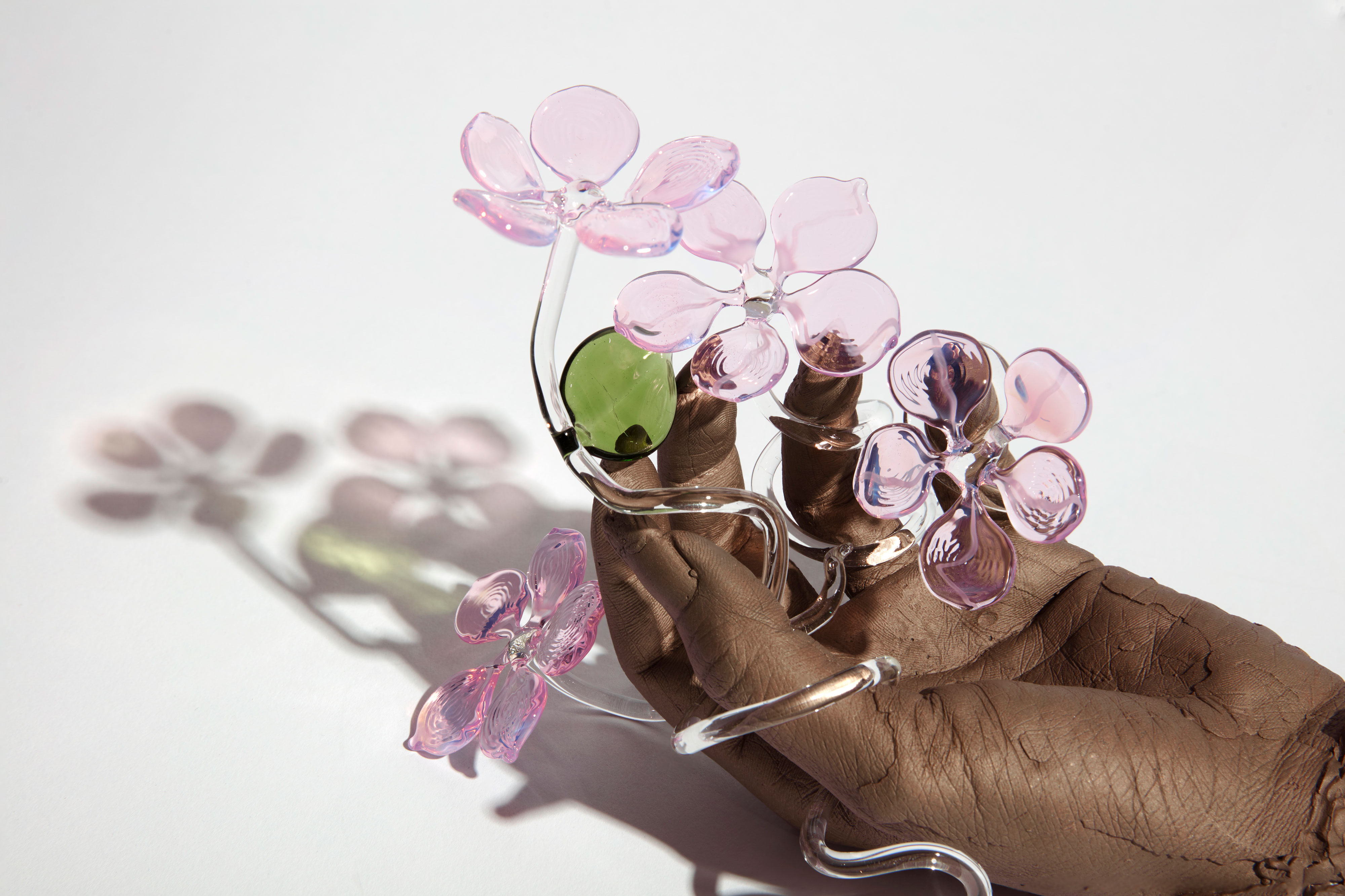 Kelly Akashi sculpture, bronze hand holding light pink glass flowers with green leaves